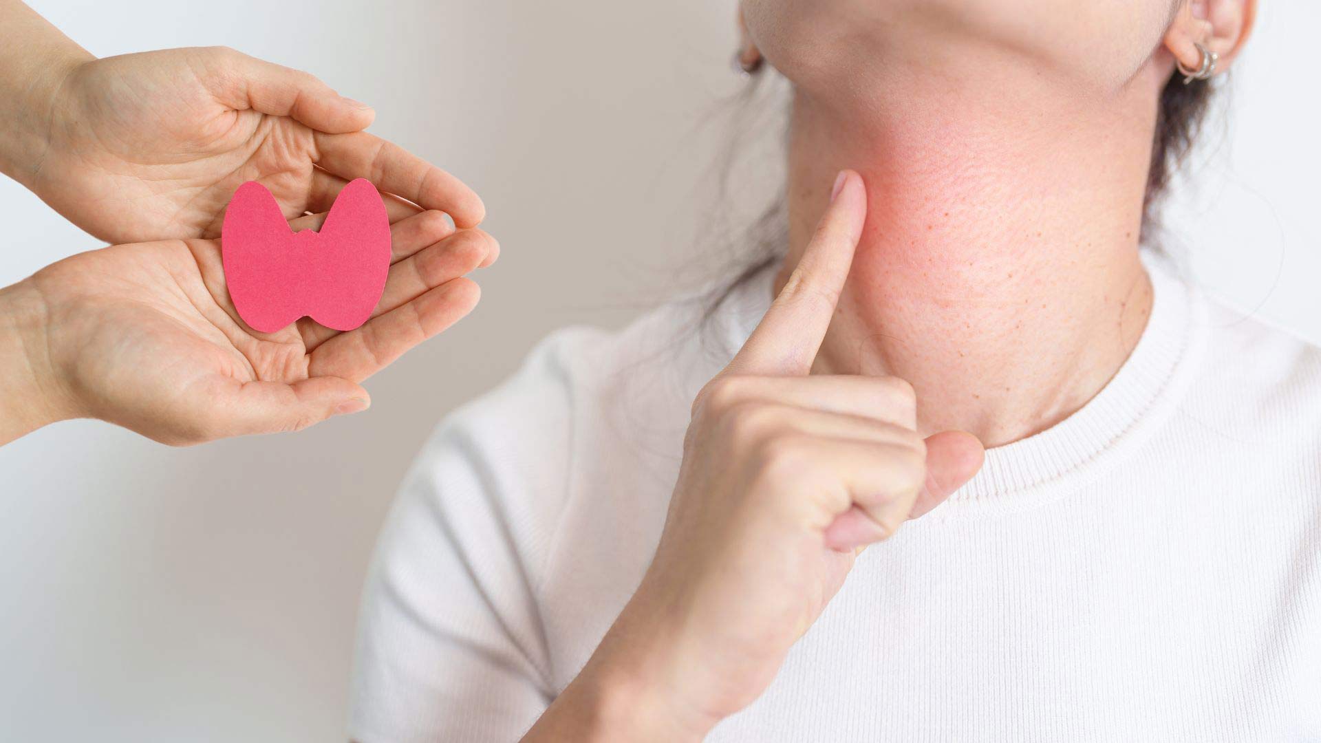 Frau zeigt auf ihre Schilddrüse