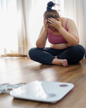 frau mit gewichtsproblemen verzweifelt vor der waage